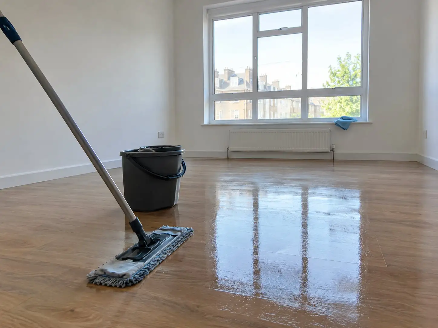 A freshly mopped floor in an empty room, with a mop and bucket