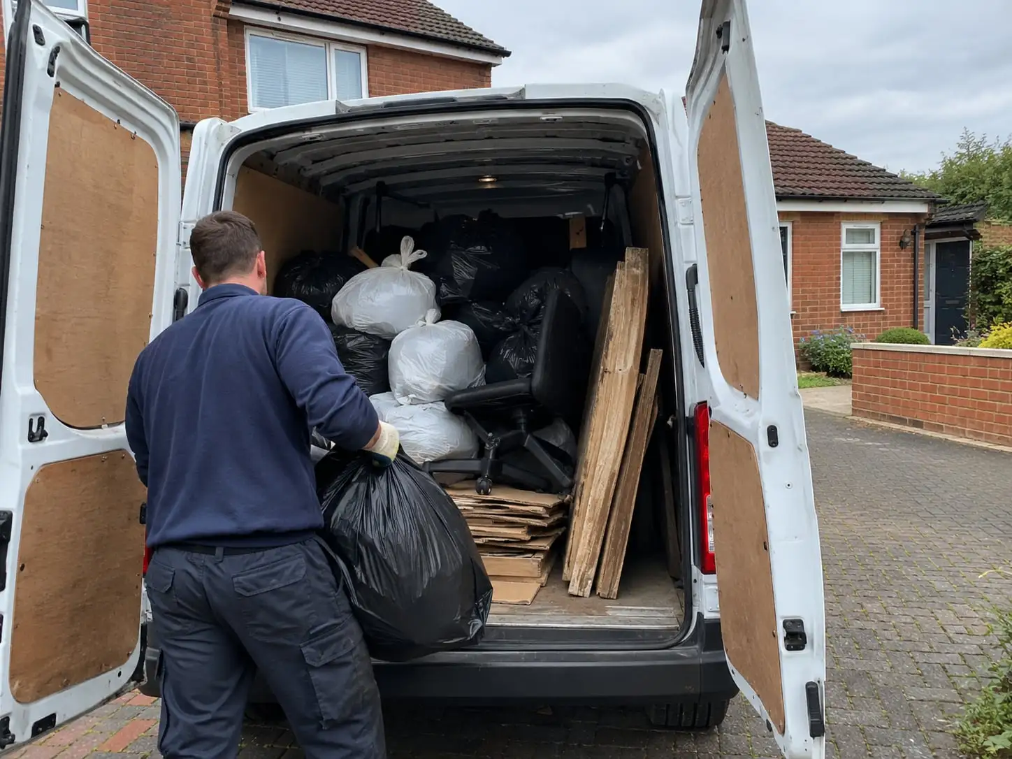A worker loading rubbish bags and old boards into a white van